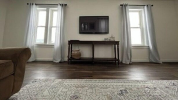 Una habitación con piso de madera, un sofá, una mesa con un televisor encima y dos ventanas con cortinas.