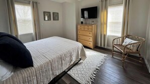 Un dormitorio con cama, cómoda, silla, ventilador de techo y televisor en la pared.