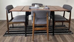 Una mesa de comedor con cuatro sillas, un tapete blanco y negro estampado, y un florero blanco sobre la mesa.