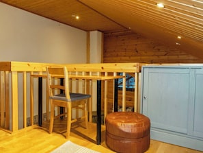 Une chambre mansardée avec une structure en bois, comprenant une chaise en bois, un pouf en cuir et une armoire bleue.