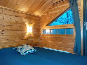 Une pièce de cabane en bois comprenant un lit, une fenêtre et une lampe fixée au mur.