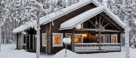 Eine Holzhütte mit Veranda, umgeben von schneebedeckten Bäumen.