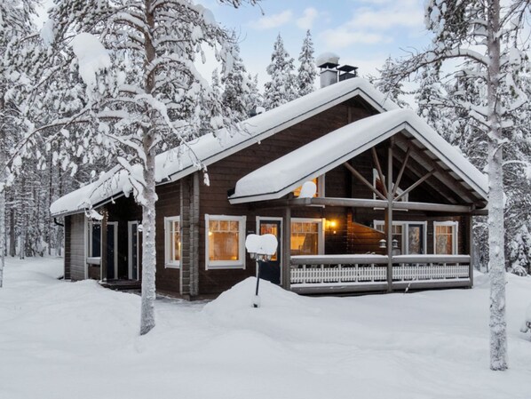 A wooden cabin with a porch, surrounded by snow-covered trees.