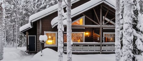 Een besneeuwde lodge met een groot raam, een veranda en een houten omheining.