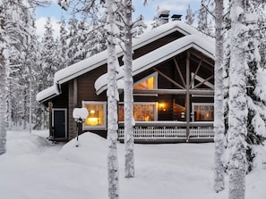 Uma cabana coberta de neve com uma janela grande, varanda e cerca de madeira.