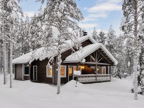 A cabin with a wooden exterior, a porch, and snow-covered trees in the background. - Apartment Ansa by Interhome (Kittilä)