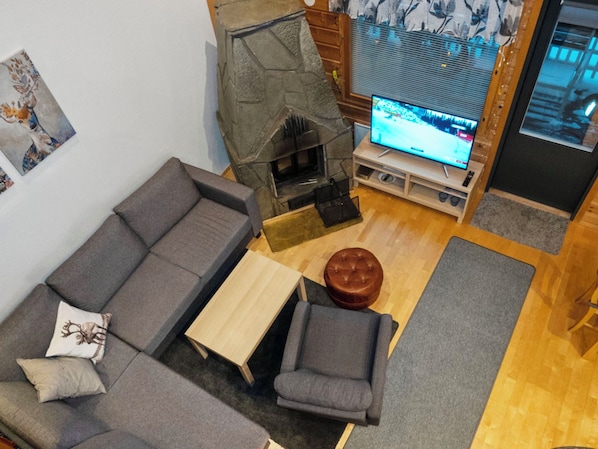 Un salon moderne comprenant un canapé d’angle, une petite table en bois, un pouf en cuir, une cheminée et un téléviseur.