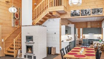Un interior espacioso con escalera de madera, chimenea, zona de comedor con mesa y sillas, y cocina con electrodomésticos modernos.