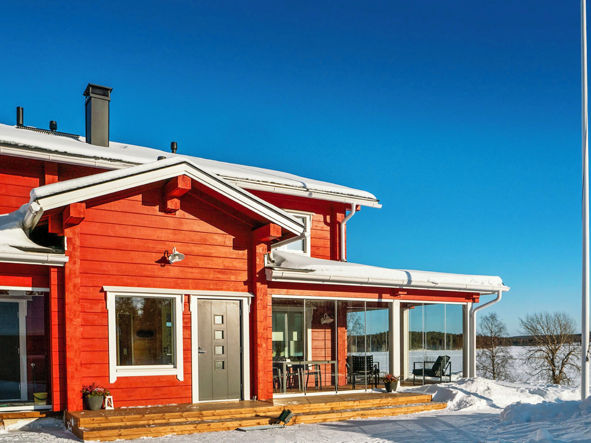 A red wooden house with a covered porch, large windows, and a chimney.