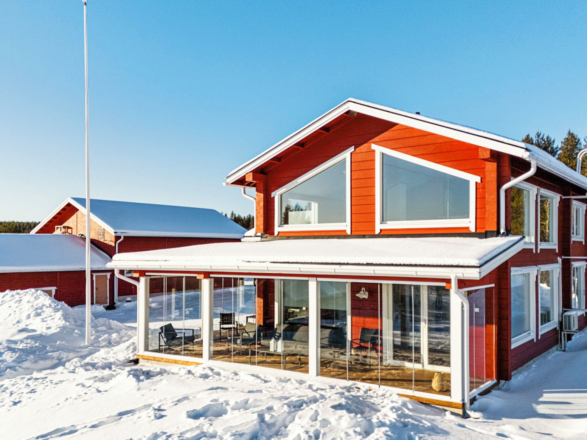 A red two-story house with a glass-enclosed porch, a flagpole, and a snow-covered landscape.