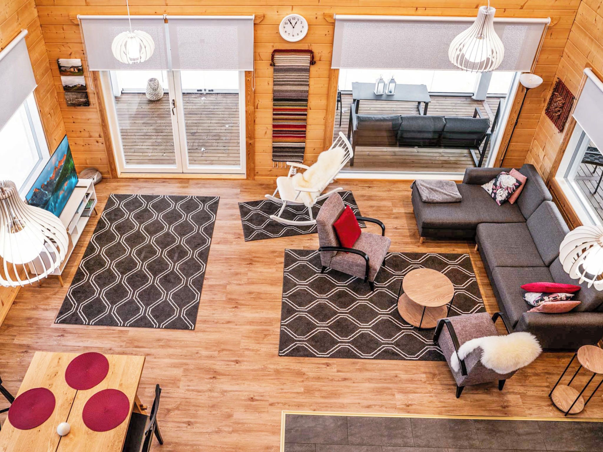 A modern interior with a sofa, rocking chair, and a dining table with red cushions.