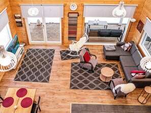 Un interior moderno con sofá, sillón mecedora y mesa de comedor con cojines rojos.