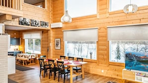 A spacious wooden cabin with a dining area, kitchen, and large windows offering scenic views.