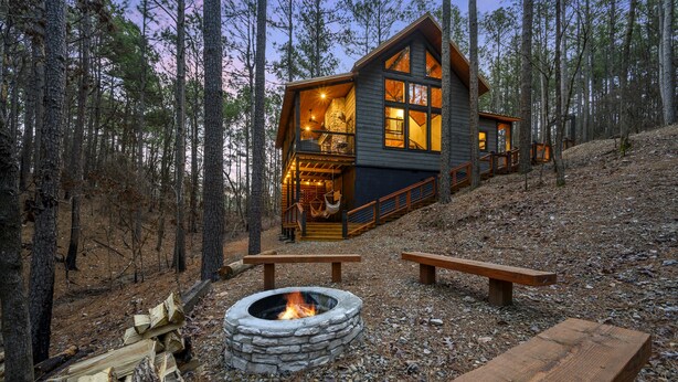 A cabin with a stone fire pit, wooden benches, and a deck. - Secluded 2 Acres • 2 King Suites • Hot Tub • Sleeps 4–8 (Broken Bow)