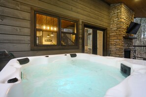 Een hottub voor een houten gebouw met een stenen schoorsteen, een raam met verlichting en een bord met de tekst 'geniet van het uitzicht'.