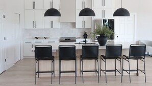 Une cuisine moderne avec des meubles blancs, des suspensions noires et un îlot central doté de tabourets de bar.