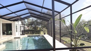 Une piscine entourée de parois en verre, une plante en pot et une vue sur l’extérieur.
