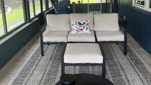 Ein überdachter Außenbereich mit einer Couch, einem Tisch, großen Fenstern und Lichterketten.