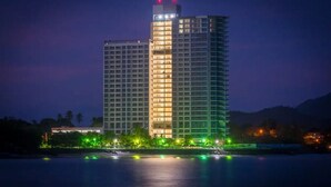 Un hotel de gran altura con varios pisos, una fachada bien iluminada y vistas a una masa de agua tranquila con reflejos.