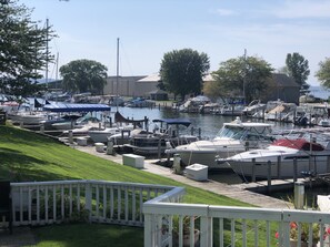 A marina with boats docked, a grassy area with a white fence, and a building in the background.