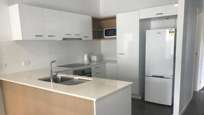 A modern kitchen with white cabinets, a stainless steel sink, a microwave, and a refrigerator.