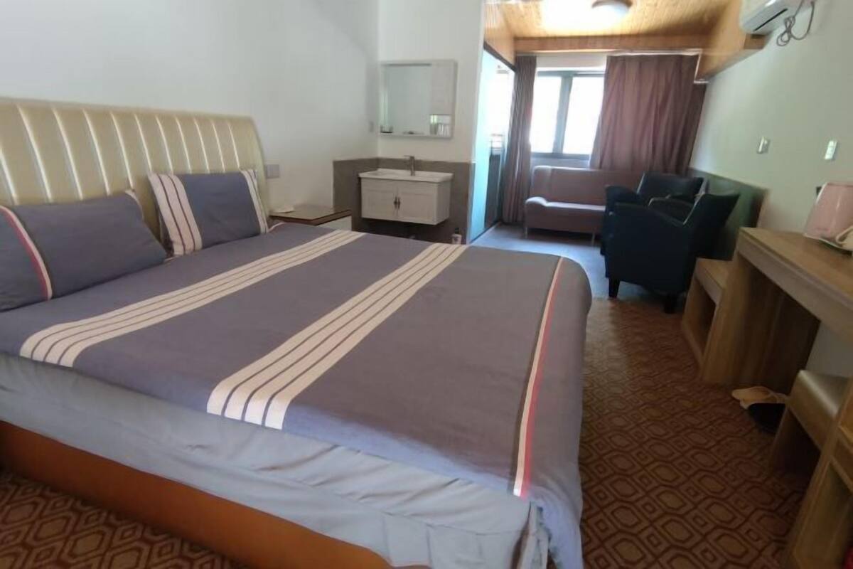Ein Hotelzimmer mit Bett, Nachttisch, Sessel, Schreibtisch, Spiegel und Fenster.