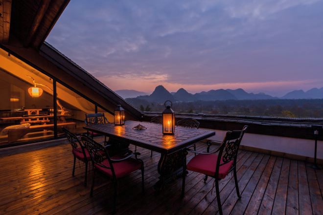 Un área de comedor al aire libre con mesa y sillas, con vistas a un río y montañas.