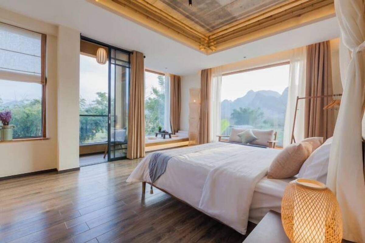 A bedroom with a large bed, a balcony with a view, and a wooden floor.