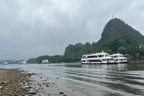 Un río con barcos, una orilla rocosa y una colina al fondo.