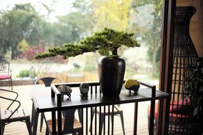 A table with a bonsai tree in a vase, chairs, and a view of a garden. - Fusheng Banri Guesthouse (Guilin Zhujiang) (Guilin)