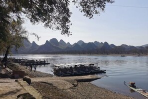 A calm lake with boats docked along the shore, surrounded by mountains. - Fusheng Banri Guesthouse (Guilin Zhujiang) (Guilin)