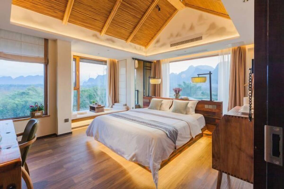 A modern hotel room with a large bed, wooden flooring, and a view of the mountains.