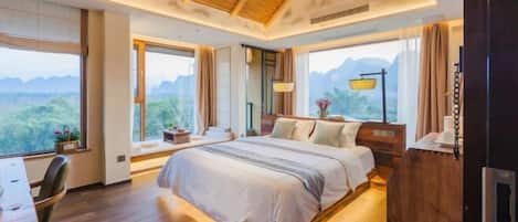 A modern hotel room with a large bed, wooden flooring, and a view of the mountains.
