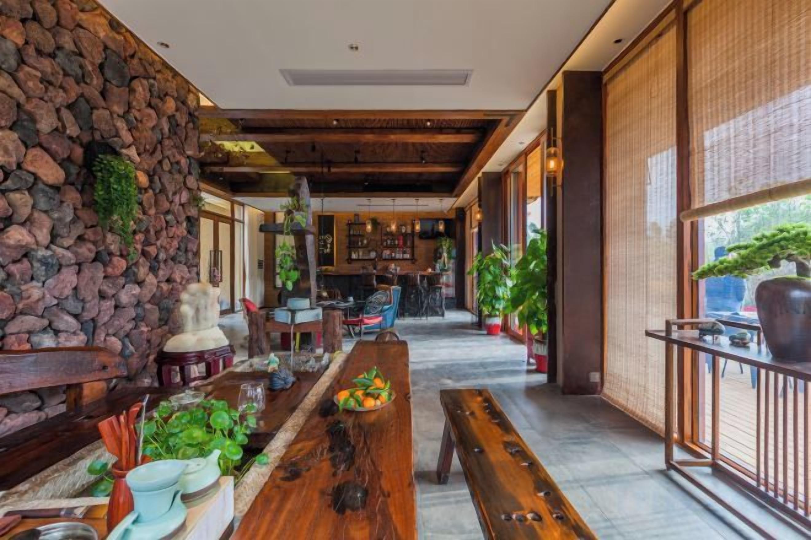 A spacious interior with a long wooden table, stone wall, and a bar area in the background.