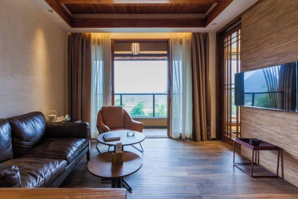 A modern living room with a leather sofa, a round coffee table, a television, and a large window with curtains.