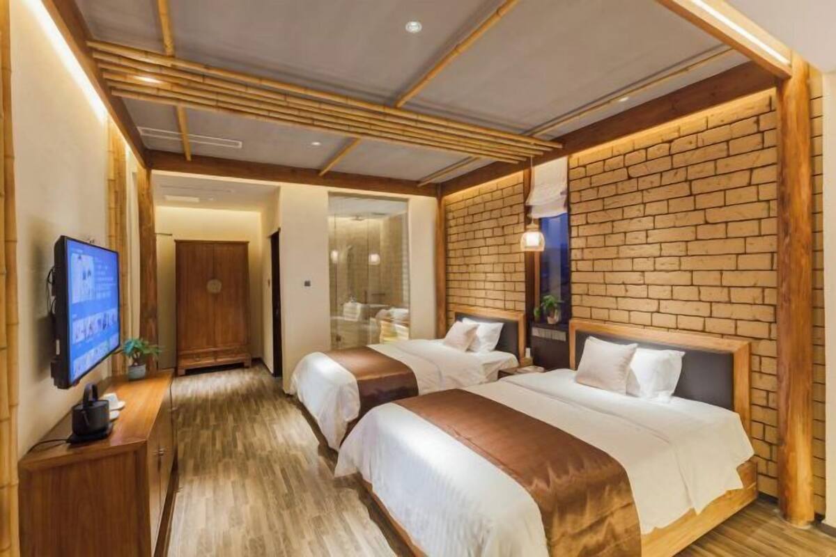 A hotel room with two beds, a TV, a wooden desk, and a brick accent wall.