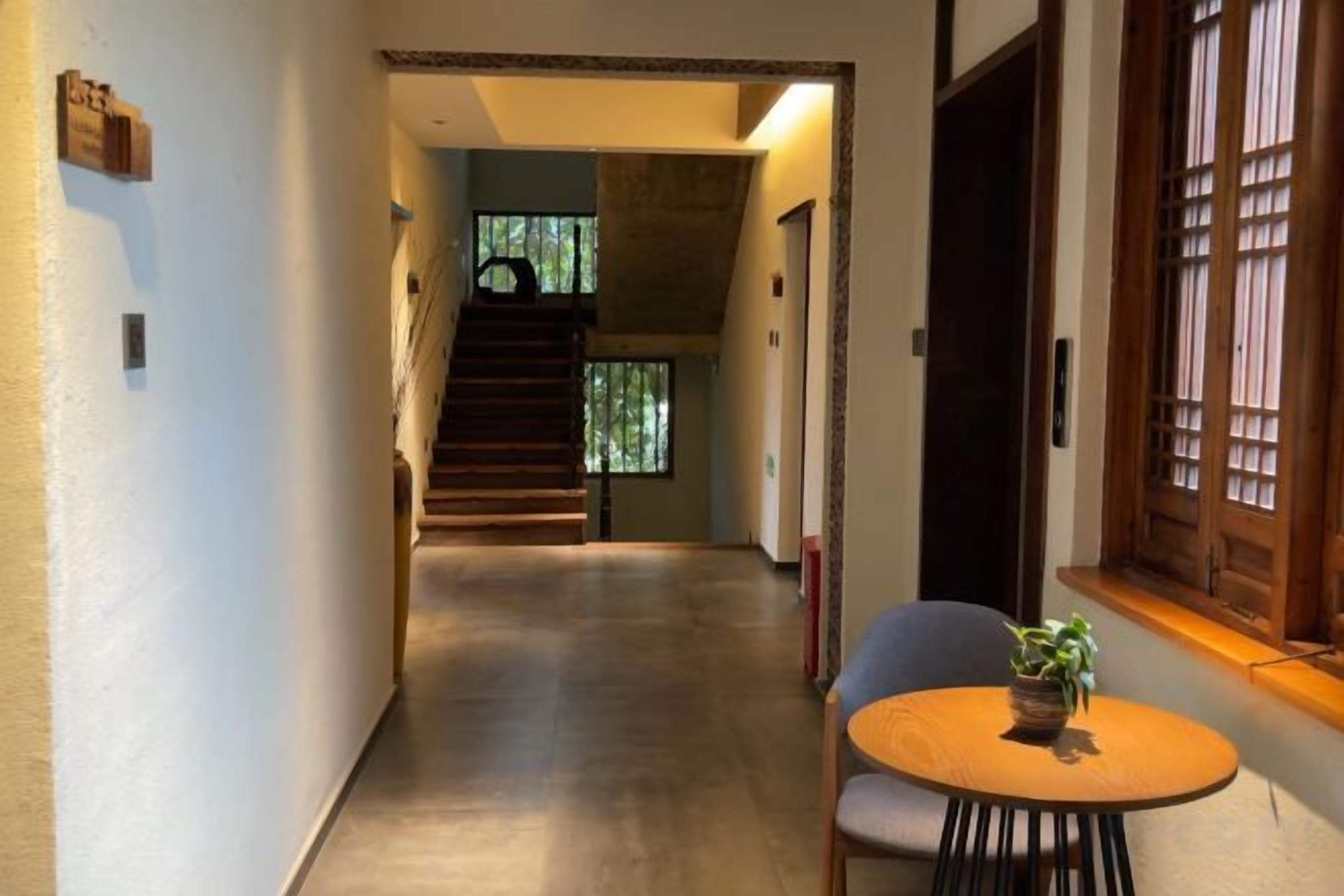 A hallway with a staircase leading to a second floor, a round table with a plant, and a window with wooden shutters.