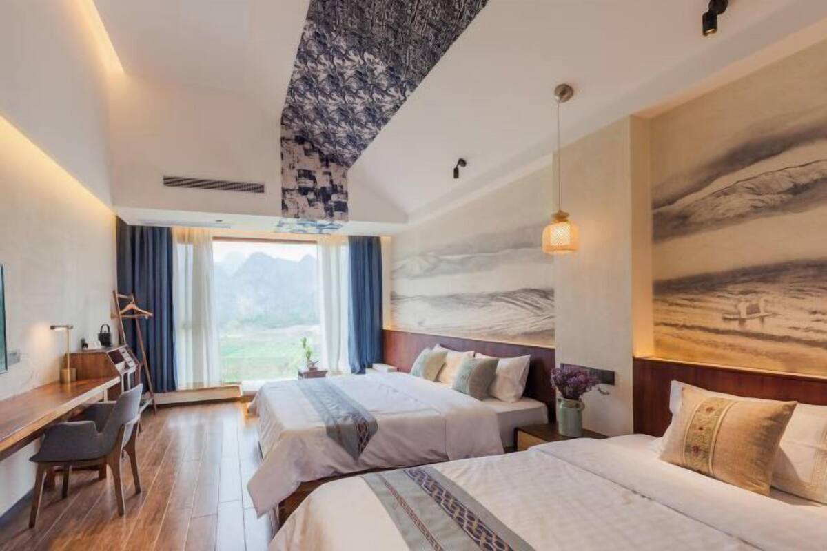 A hotel room with two beds, a desk, a chair, and a large window with curtains.