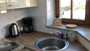 A kitchen with a stainless steel sink, a coffee maker, and a window with a view of the outdoors.