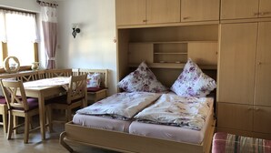A room with a wooden bed, a wooden desk with a chair, a small table, and a window with curtains.
