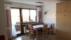 A dining area with a wooden table and chairs, a window with curtains, and a wooden wardrobe.