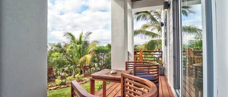 A wooden deck with outdoor seating, a glass door, and a view of a tropical garden.