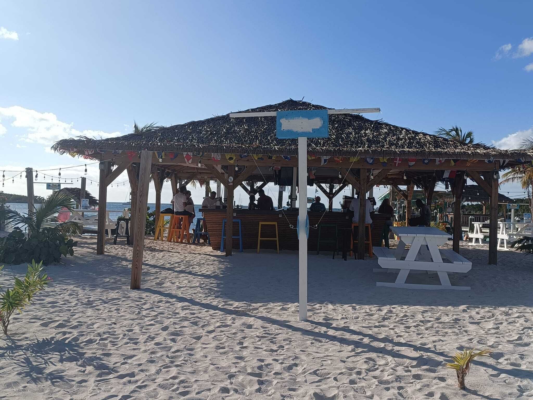 A beachside pavilion with a thatched roof, seating, and a table.