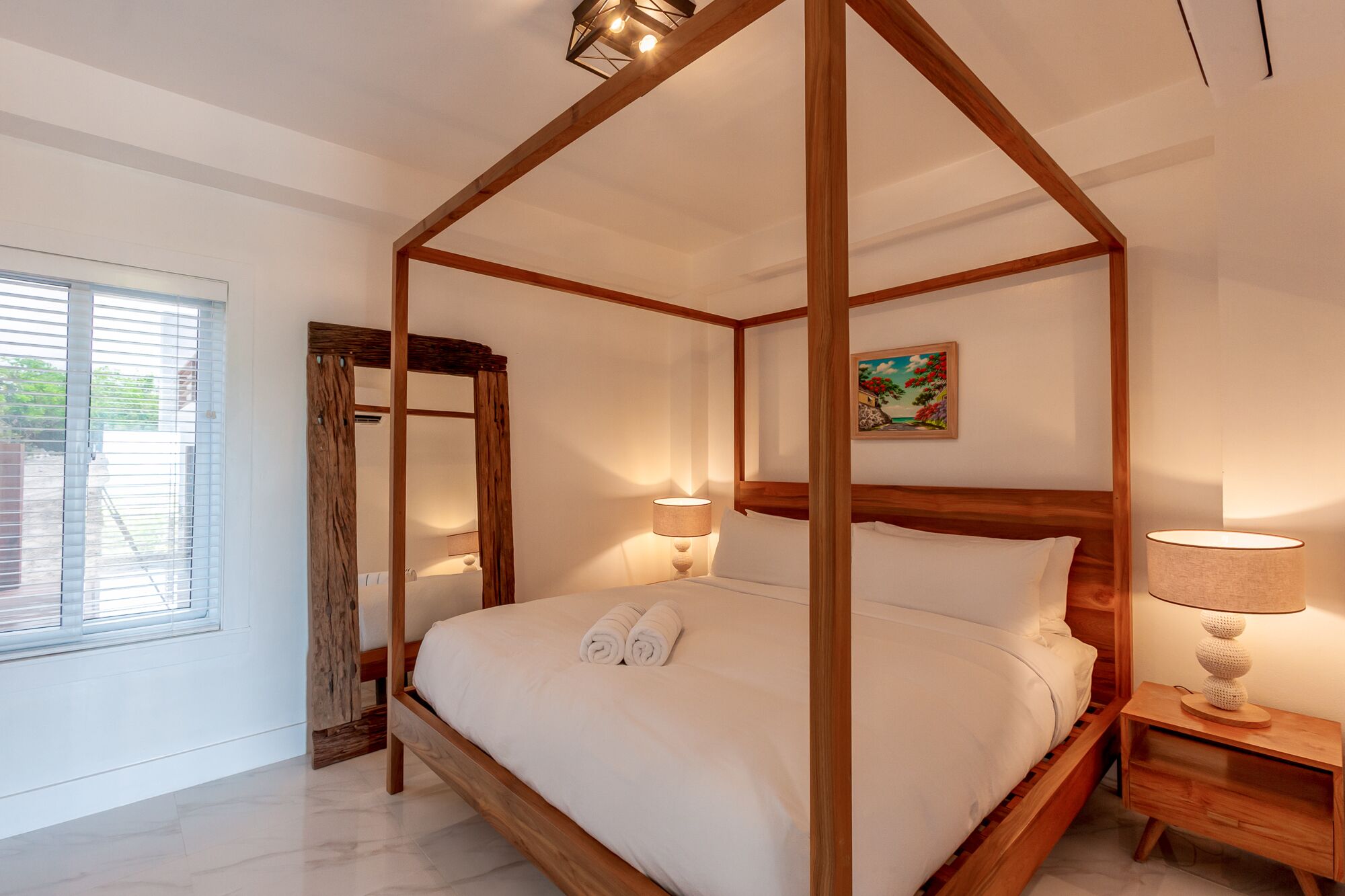 A four-poster bed with white linens, two bedside lamps, and a painting on the wall.
