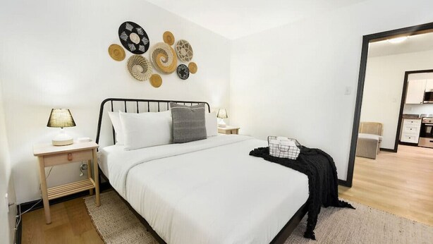 Un dormitorio moderno con una cama grande, dos mesitas de noche con lámparas, un plaid negro y un cuadro en la pared.