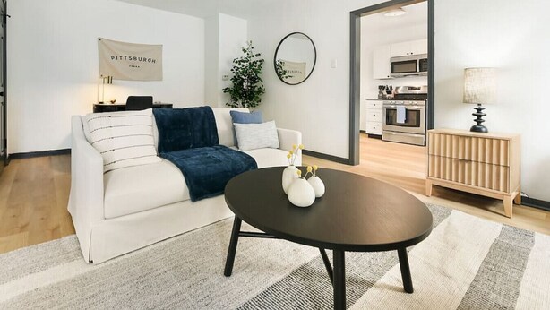 En moderne stue med en hvid sofa, et mørkt rundt sofabord og et spejl på væggen.