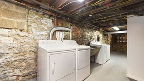 Et vaskerum med stablede vaskemaskiner og tørretumblere, stenvægge, synlige ventilationskanaler og en beton gulv.