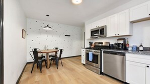 Et moderne køkken med hvide skabe, rustfrie stål-apparater og et spiseområde med et bord og stole.