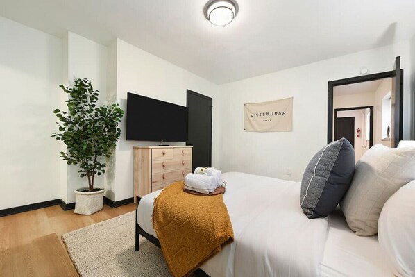 A modern hotel room with a bed, a TV, a dresser, a potted plant, and a sign on the wall. - ★ HostWise Stays ★ Pet Friendly, Butler St. Apt with Private Entrance (Pittsburgh)