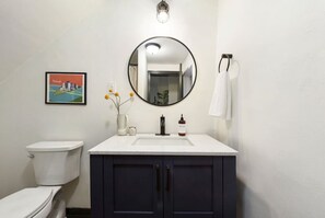 A bathroom with a toilet, a sink with a mirror, a framed picture, and a vase with flowers. - ★ HostWise Stays ★ Pet Friendly, Butler St. Apt with Private Entrance (Pittsburgh)